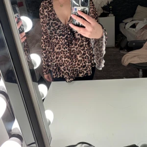 Leopardmönstrad blus med knyt - Säljer en snygg leopardmönstrad blus med v-ringning och knyt framtill. Blusen har långa ärmar och är perfekt för en trendig look. Passar bra till både jeans och kjol.