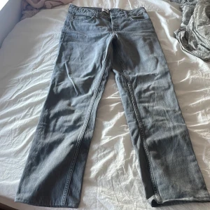 Grå jeans från 157 - Snygga grå jeans från 157 med en klassisk femficksdesign. De har en knappgylf och bälteshällor, vilket gör dem perfekta för en avslappnad stil. Passformen är rak och de är tillverkade i ett slitstarkt material.