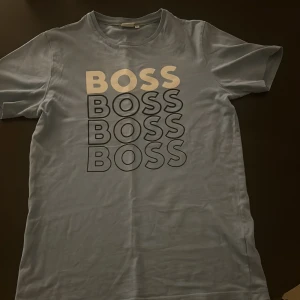  t-shirt från Boss - Snygg ljusblåt-shirt från Boss med tryck i flera nyanser av grått och vit. Perfekt för en avslappnad stil. Kortärmad och tillverkad i mjukt material.