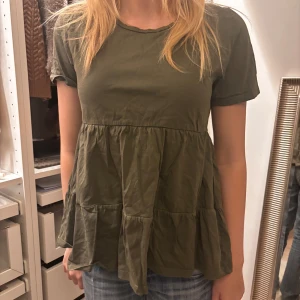 Olivgrön blus - Säljer en söt olivgrön blus med korta ärmar och volangdetaljer. Perfekt för en avslappnad stil. Blusen har en luftig passform och är tillverkad i ett mjukt material.