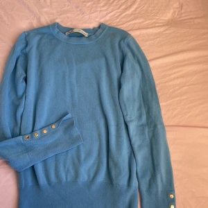 Blå tröja från Zara - Säljer en snygg blå tröja från Zara med långa ärmar och dekorativa guldknappar vid ärmsluten. Perfekt för en vardags outfit!  Pris kan diskuteras❤️