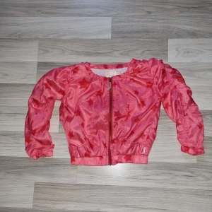 Rosa jacka med stjärnor från Aya Naya - Säljer en söt rosa jacka från Aya Naya med stjärnmönster. Jackan har en dragkedja framtill och långa ärmar. Insidan är fodrad med ett ljust tyg med små rosa mönster. Perfekt för att liva upp garderoben! 🌟