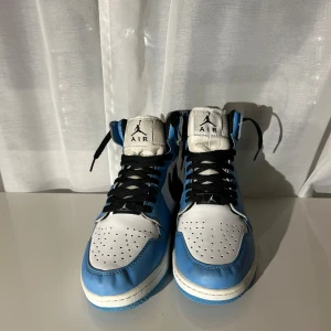 Nike Air Jordans i blått och vitt - Snygga Nike Air Jordans i en fräsch blå och vit färgkombination. Skorna har klassisk snörning och en hög siluett med den ikoniska Air Jordan-loggan på sidan. Perfekta för att ge din outfit en sportig touch.