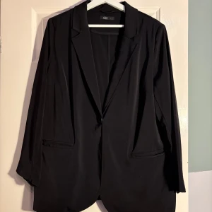 Svart kavaj från xlnt - Snygg svart kavaj från xlnt i storlek L. Den har en klassisk design med långa ärmar och en enkel knapp framtill. Perfekt för en stilren look.