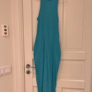 Turkos ribbad långklänning - Snygg turkos ribbad långklänning med cut-out detaljer i ryggen. Perfekt för en somrig look. Klänningen är ärmlös och har en figurnära passform som framhäver silhuetten.