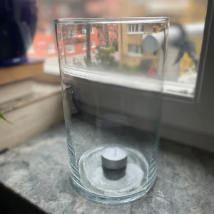 Glasvas eller vindskydd till ljus - Säljer en stilren glasvas som även kan användas som ljuslykta. Vasen är cylindrisk och genomskinlig, vilket gör den lätt att matcha med olika inredningsstilar.