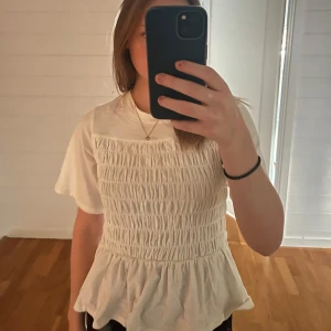 Vit smockad topp - Säljer en söt vit smockad topp med volangdetalj i nederkant. Toppen har korta ärmar och en bekväm passform.