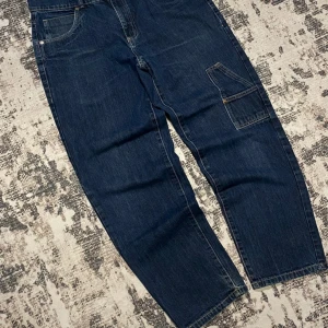 Southpole baggy jeans - Snygga mörkblå jeans från Southpole med en urban stil. De har en loose passform och är dekorerade med ett stort tryck på bakfickan. Perfekta för en avslappnad look. #emo #y2k #drainer #opium