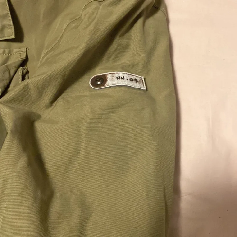 Säljer en grön jacka från NN.07 i bra skick. Den har en dragkedja och knappar framtill, samt flera praktiska fickor. Perfekt för höst och vår med sin stilrena design och bekväma passform. Insidan är fodrad med mjukt material för extra komfort. Har luva också som man kan väckla in i jackan. Pris är inte hugget i sten. Takit.