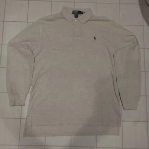 Beige pikétröja från Ralph Lauren - Säljer en klassisk beige pikétröja från Ralph Lauren med den ikoniska loggan broderad på bröstet. Tröjan har långa ärmar och en stilren krage med knappar. Perfekt för en avslappnad men ändå stilfull look.