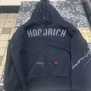 Svart hoodie från Hoodrich - Säljer en svart hoodie från Hoodrich med texten 'FROM NOTHING TO SOMETHING' på baksidan och 'HOODRICH' på framsidan. Hoodien har en stor ficka framtill och justerbar huva med snören. Perfekt för en avslappnad stil.