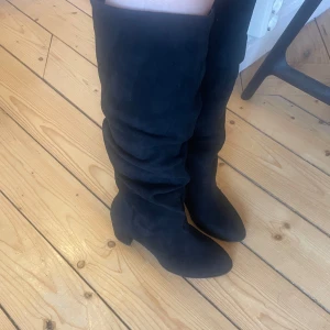 Svarta boots i mocka imitation - Snygga svarta stövlar i mocka med en stilren design. De har en hög skaft och en bekväm klack som ger en elegant look. Perfekta för att komplettera din outfit under kyligare dagar.