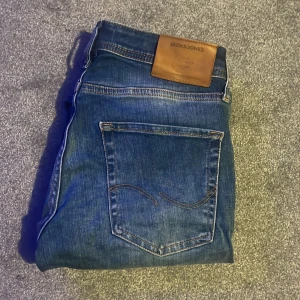 Blå jeans från Jack & Jones - Snygga blå jeans från Jack & Jones med klassisk femficksdesign. De har en knappgylf och en läderpatch med logotyp baktill. Perfekta för en avslappnad stil. Dem är i passformen slim