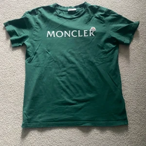 Grön Moncler T-shirt - Säljer denna snygga gröna Moncler T-shirt som är i bra skick men ett litet hål på framsidan på T-shirten  som man ser på en av bilderna men skriv om du vill ha en närmare titt på tröjan. 