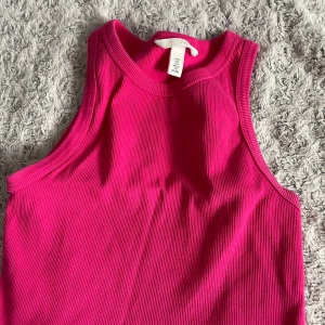 Rosa ribbad linnetopp från H&M - Säljer en snygg rosa ribbad linnetopp från H&M. Toppen är ärmlös och har en rund halsringning, perfekt för varma dagar. Den är tillverkad i ett mjukt och stretchigt material som ger en bekväm passform.