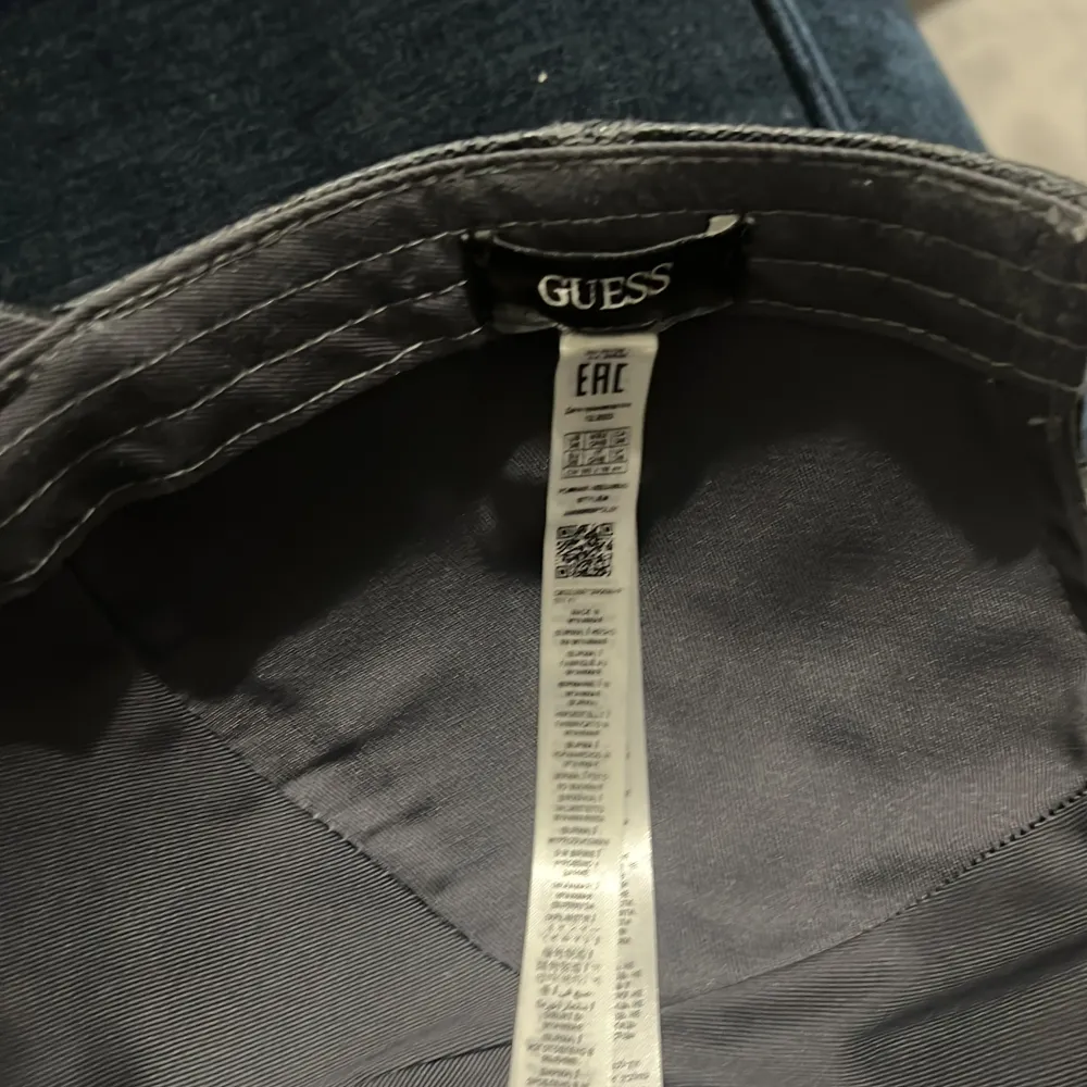 Snygg svart keps från Guess med ett diskret mönster och metallogo framtill. Kepsen har justerbar rem baktill för perfekt passform.. Asusteet.