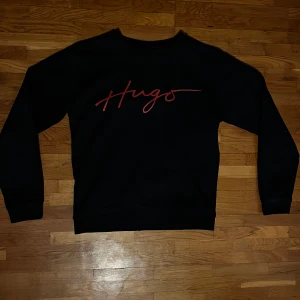 Svart tröja från Hugo  - Snygg svart tröja från Hugo med röd text på bröstet. Perfekt för en stilren look. Tröjan har långa ärmar och en klassisk passform.