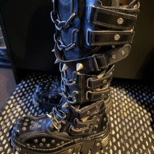 New rock boots  med kedjor och nitar  - Säljer ett par svarta boots från New Rock med kedjor och nitar. De har en robust sula och flera spännen för en unik look. Perfekta för dig som vill ha en edgy stil.
