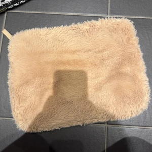 Beige pälsig datorfodral från H&M - Mysig beige datorfodral från H&M med en fluffig pälsig yta. Väskan har en dragkedja upptill för säker förvaring. Perfekt för att ge en trendig touch till din outfit. Den är 26x34 cm 
