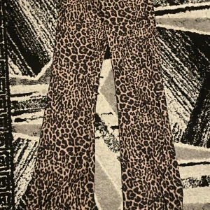 Leopardmönstrade byxor från F&F - Snygga leopardmönstrade byxor från F&F i en tight passform. Byxorna har en hög midja och vida ben, vilket ger en trendig look. Perfekta för att sticka ut med ett djärvt mönster.