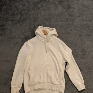 Vit hoodie - Säljer en stilren vit hoodie med praktisk huva. Perfekt för en avslappnad look. Den har en klassisk passform och är tillverkad i ett mjukt material för extra komfort.