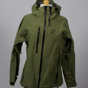 Grön jacka - RevolutionRace friluftsjacka i storlek Large. Oanvänd! Damjacka med recco reflector på armen, recco reflectorn sitter fel (produktionsfel)  🔹 Färg: Grön 🔹 Storlek: Large 🔹 Skick: Oanvänd (produktionsfel)  🔹 Rek. nypris: 1 499 kr – Vi säljer för 450! 💚 Om oss: Reclaims UF samarbetar med kända varumärken för att rädda kläder från att slängas. Vi fixar till dem och ger dem en ny chans – hållbart, snyggt och prisvärt! 📦 Frakt: Skickas med PostNord/Schenker inom 1–3 dagar