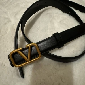 Svart skärp med guldfärgat spänne - Snyggt svart skärp i skinn med ett stilrent guldfärgat spänne. Perfekt för att ge en elegant touch till din outfit. Skärpet har flera hål för justerbar passform.