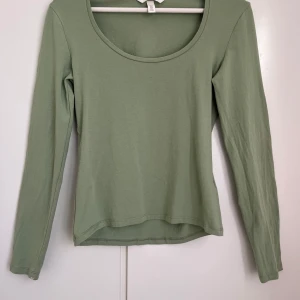 Grön långärmad tröja från H&M - Snygg och enkel grön långärmad topp från H&M. Perfekt för en avslappnad stil med rund halsringning och mjukt material. Passar bra till jeans eller kjol för en stilren look.