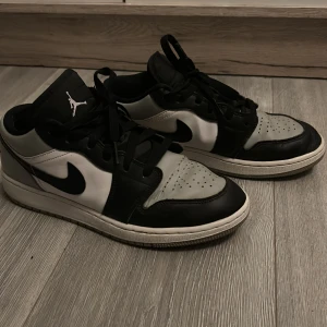 Air Jordan 1 Low  - Snygga Air Jordan 1 Low 'Shadow Toe' sneakers i svart, vit och grå. Skorna har en klassisk design med snörning och den ikoniska Nike-loggan på sidan. Perfekta för dig som vill ha en stilren och sportig look.