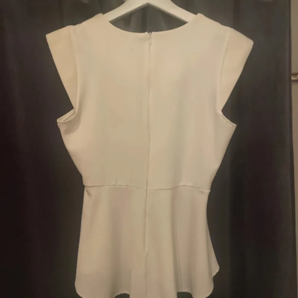 Säljer en stilren vit blus från VILA i storlek S. Blusen har en elegant design med ärmlös stil och en lätt utsvängd nederdel. Dragkedja på ryggen. Axlarna på blusen är fylliga. Blusen är använd 2 gånger.. Puserot.