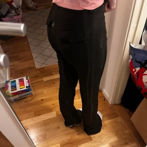 Svarta kostymbyxor från Gina Tricot - Snygga svarta kostymbyxor från Gina Tricot med hög midja och bootcut-stil. Byxorna har knappar framtill och en stilren design som passar perfekt för en chic look.