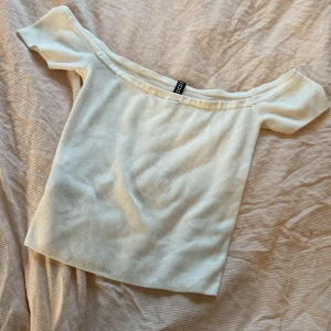 Vit offshoulder topp från Divided - Säljer en stilren vit offshoulder topp från Divided. Toppen har en ribbad struktur och korta ärmar, perfekt för en somrig look. Passar bra till både jeans och kjol. Hör av dig vid intresse! Sitter som en smäck på koppen. 
