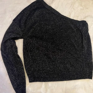 Svart glittrig offshoulder tröja från NA-KD - Snygg svart glittrig tröja från NA-KD i offshoulder-modell. Perfekt för att sticka ut med sin glittriga yta. Tröjan har långa ärmar och en bekväm passform. Perfekt för en kväll ute eller en speciell tillställning. ✨mjuk och tunn, ej genomskinlig. Använd fåtal gånger
