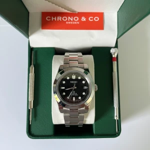 Black Oyster - Seiko Mod  - Klockan är i nyskick, precis modifierad och byggd av oss. Utrustad med ett automatiskt urverk från Seiko NH35. Klocklåda samt verktyg för att ta bort länkar medföljer.  Vid frakt, packar vi klockan säkert. Hör av er vid fler frågor/bilder!