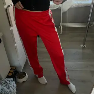 Röda coola byxor från adidas i träningsmaterial Storlek S (jag på bilden är 172 och de sitter perfekt) Några små fläckar på de vita ränderna (se sista bild) men inga stora fläckar eller hål som syns Nypris ligger på 829, sänkt priset pga av fläckar