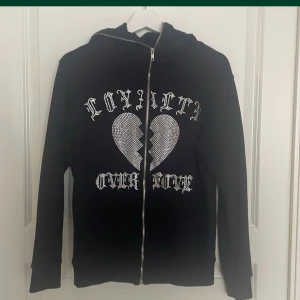 Trotherz zip up hoodie i XS - Trotherz svart zip up hoodie med dragkedja framtill. Dragkedjan går hela vägen på luvan. Motiv med strass på framsidan: loyalty over love. Bra skick. Djur- o rökfritt hem.
