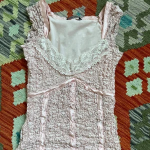 Rosa spetslinne från Dunnes Stores - Säljer ett supergulligt rosa spetslinne från Dunnes Stores. Det har en vacker spetsdetalj vid halsringningen och är ärmlöst. Perfekt för sommardagar eller en festlig kväll. Linnet är i bra skick och redo för nya äventyr!