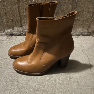 Bruna skinnstövletter med klack 36 Oanvända - Säljer ett par snygga bruna skinnstövletter. De har en bekväm klack och dragkedja på sidan för enkel på- och avtagning. Perfekta för höst och vinter, och de funkar lika bra till vardags som till fest. Skorna är i bra skick och redo för nya ävent