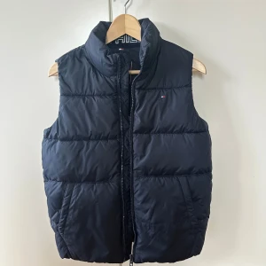 Ny mörkblå dunväst från Tommy Hilfiger - Snygg mörkblå dunväst - aldrig använd. Därav skick 10/10. Strl 152, men är ganska stor i storleken. Passar någon som är ca 155-165 cm lång.