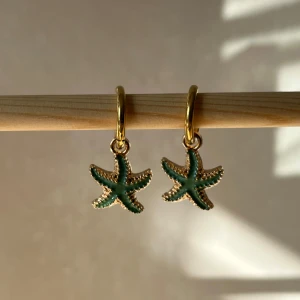 Guldörhängen med sjöstjärna - Superfina guldörhängen med en grön sjöstjärna som hänge. Perfekta för att ge en somrig touch till din outfit. De är både stilrena och unika, och passar perfekt för både vardag och fest. Köp dem och känn dig som en havsgudinna! 🌊✨helt ny handgjorda 