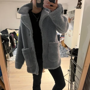 Ljusblå teddyjacka från Monki - Mysig ljusblå trendig teddyjacka från Monki i storlek XXS. Jackan har en fluffig textur och stora fickor framtill. 