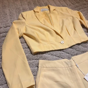 Gul croppad kavaj och byxor från NLY Trend - Snygg gul kostym från NLY Trend med croppad kavaj och matchande byxor. Kavajen har en knapp framtill och byxorna har en dragkedja och knappstängning. Perfekt för en stilren look.