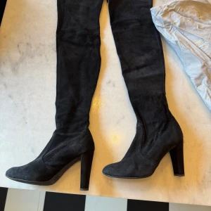 Svarta mockastövlar från Stuart Weitzman - Snygga svarta stövlar i mocka från Stuart Weitzman med hög klack och spetsig tå. Perfekta för en elegant look. Stövlarna har en stilren design och är knähöga. Välanvända men fortfarande mycket att ge. Fler bilder kan skickas. Ny pris ca 10 000 kr