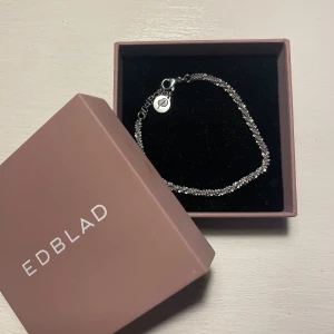 Silverfärgat armband från Edblad - Elegant silverfärgat armband från Edblad. Armbandet har en diskret kedja och en liten rund berlock med Edblads logga. 
