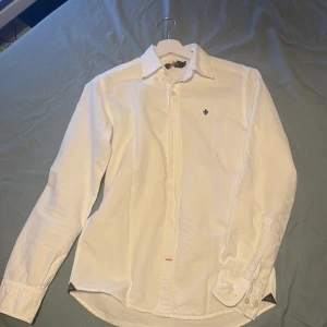 Vit skjorta från Morris - Säljer en stilren vit skjorta från Morris i storlek XS. Skjortan har långa ärmar och klassiska knappar framtill. Perfekt för en elegant look. Liten skråma vid storleks patchen men annars en är sicket 9/10 