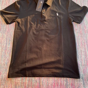 Polo Raulph Lauren shirt - ✔ Märke: Polo Ralph Lauren ✔ Modell: Pikétröja ✔ Färg: Svart ✔ Storlek: Medium (M) ✔ Material: Högkvalitativ bomullsmesh – andas och är bekväm ✔ Passform: Allt från 165-183cm 60-80kg beroende på hur man vill den ska sitta.