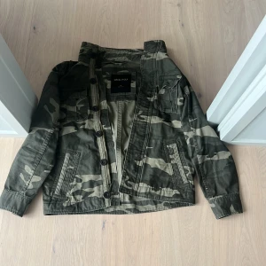 Field Jacket - Säljer en cool camouflagejacka från Cruel Wolf. Jackan har en klassisk militärlook med knappar framtill och flera praktiska fickor. Perfekt för en avslappnad stil. Perfekt nu för våren 💯💯