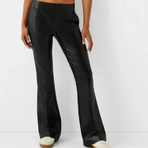 Lågmidjade Skinnbyxor - Snygga svarta bootcut byxor i syntetmaterial. De har en stilren design med en lågmidjad passform som ger en elegant siluett. Perfekta för att skapa en chic look.