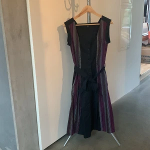 Randig klänning med knytband och fickor  - Snygg bomullsklänning med randigt mönster i lila och svart. Den har ett knytband i midjan, fickor och knappar framtill. Perfekt för en stilren look. Malmö-märke PicaPica, som tyvärr inte gör kläder längre. Underbar klänning!