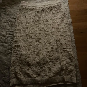 Beige stickad kjol - Mysig beige stickad kjol med ett diskret mönster. Perfekt för kyligare dagar med sin mjuka och bekväma passform. Kjolen har en elastisk midja för extra komfort.